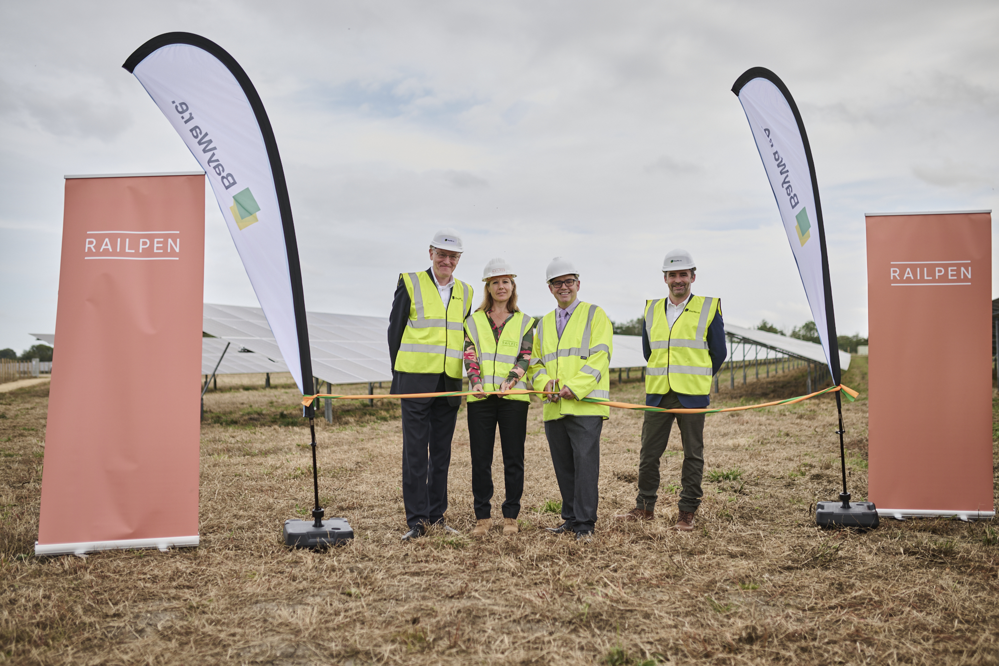 4 people in hard hats and high-vis cut ribbon in front of solar farm